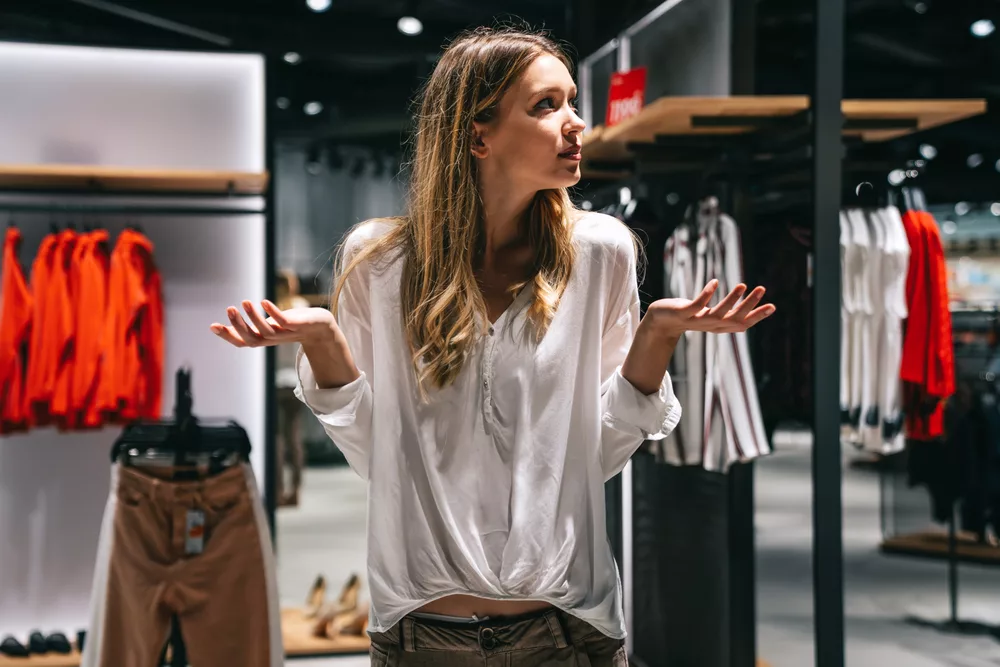 Jeune femme en hésitation dans un magasin de prêt-à-porter